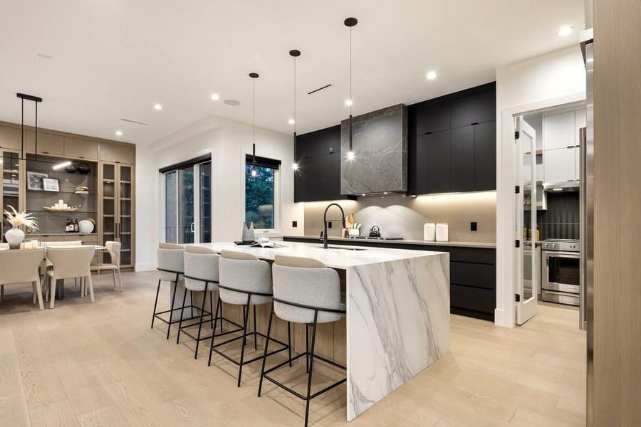 Compact open kitchen with a sleek marble island, black cabinets, and modern pendant lighting.
