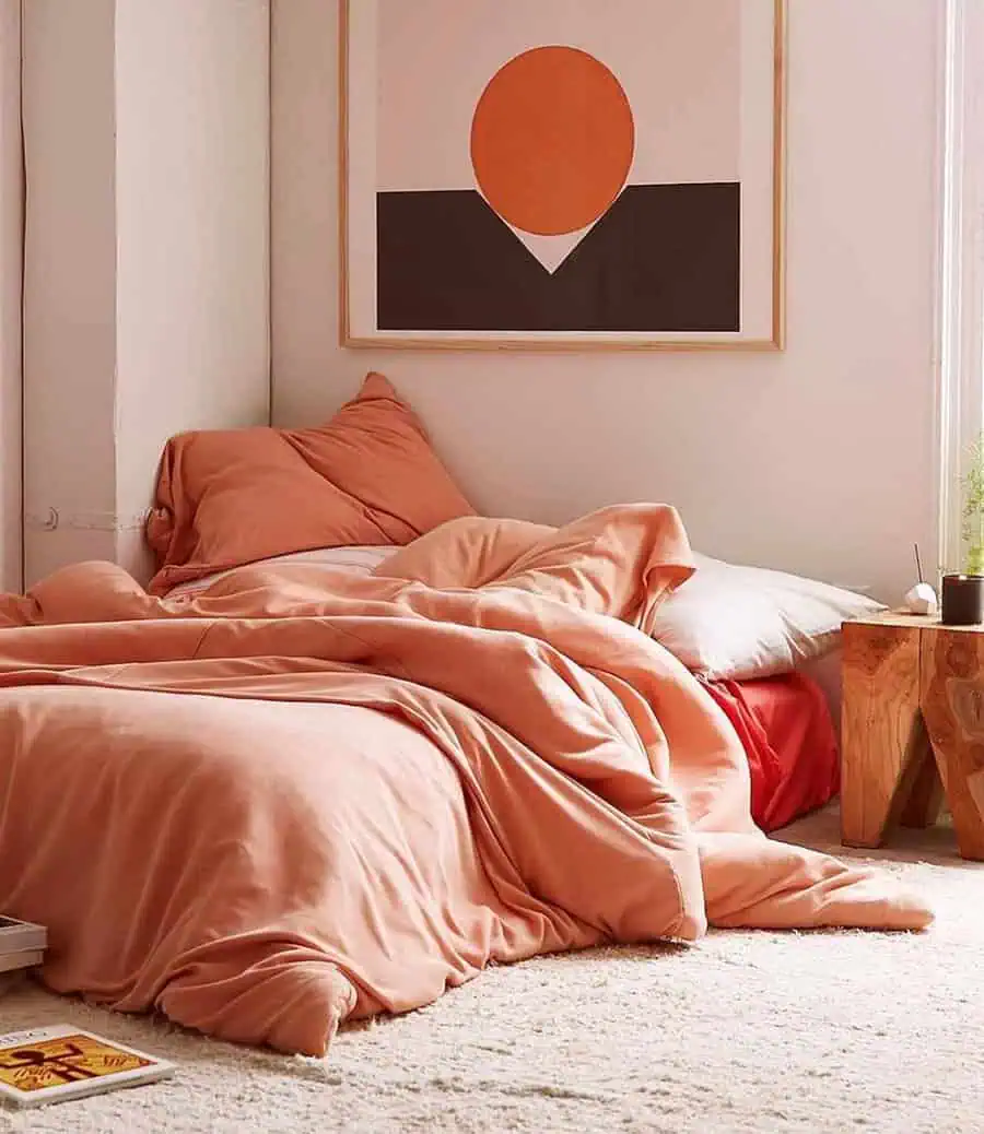 Cozy bedroom with warm orange bedding, soft textures, wooden accents, and minimalist decor.