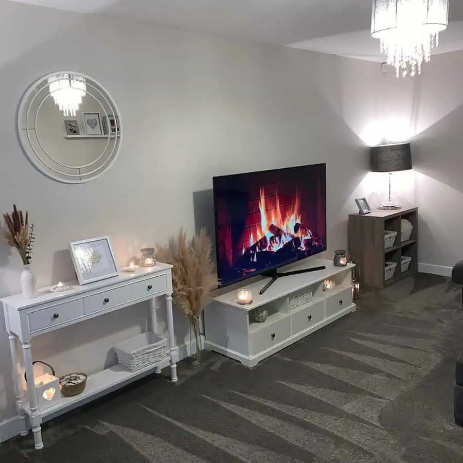 Cozy grey and white living room with a TV fireplace display, candles, and elegant decorative accents.