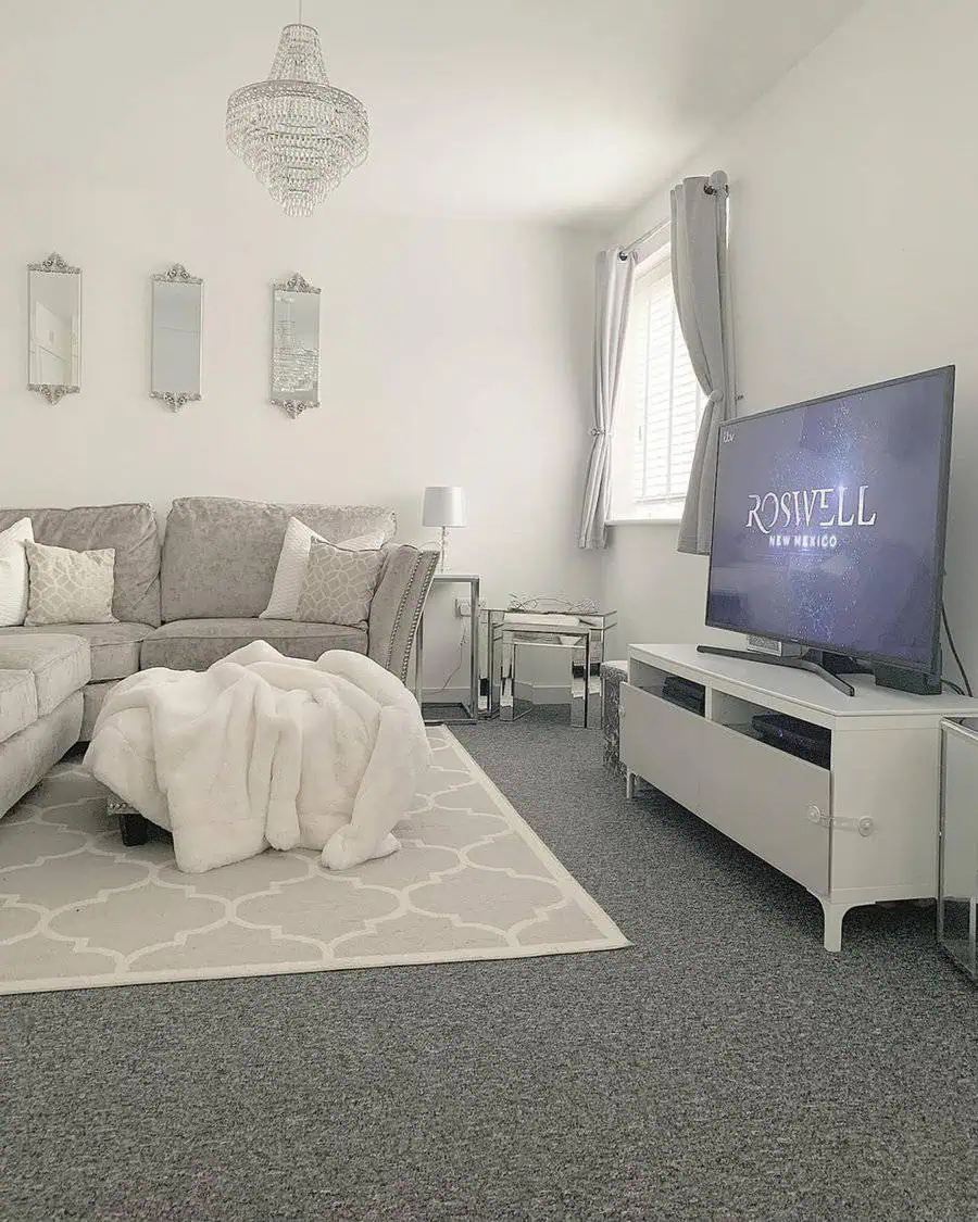 Elegant grey and white living room with a plush sofa, crystal chandelier, and soft decorative accents.