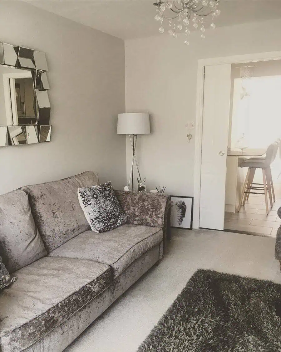 Grey and white living room with a plush sofa, mirrored wall decor, and a crystal chandelier.