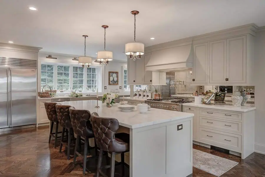 Elegant open kitchen with custom cabinetry, a large marble island, and tufted leather bar stools.