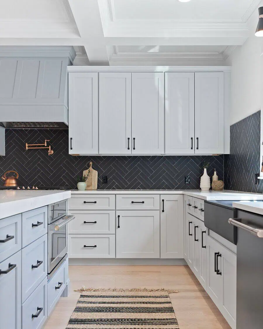 Black herringbone backsplash adds bold contrast to white cabinets for a modern, sophisticated kitchen.