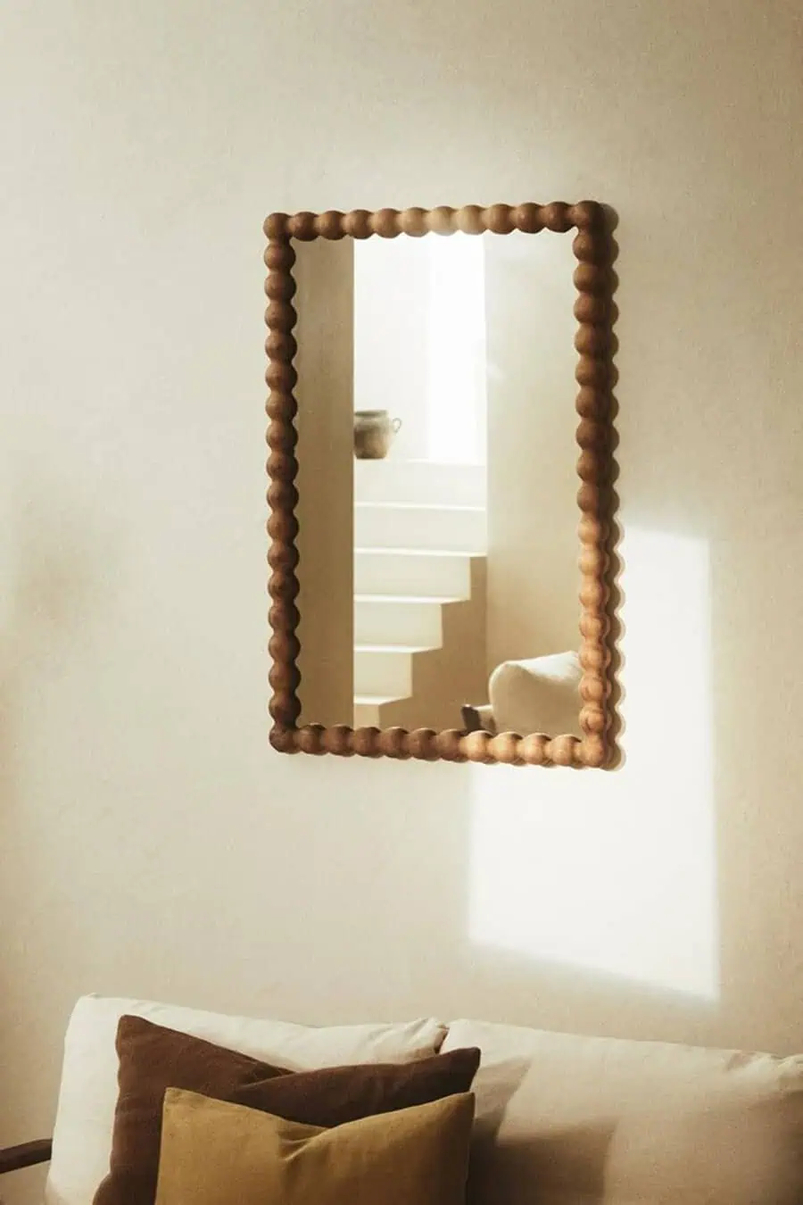 Decorative bead-edged mirror reflecting a cozy living room with earthy tones and natural light.