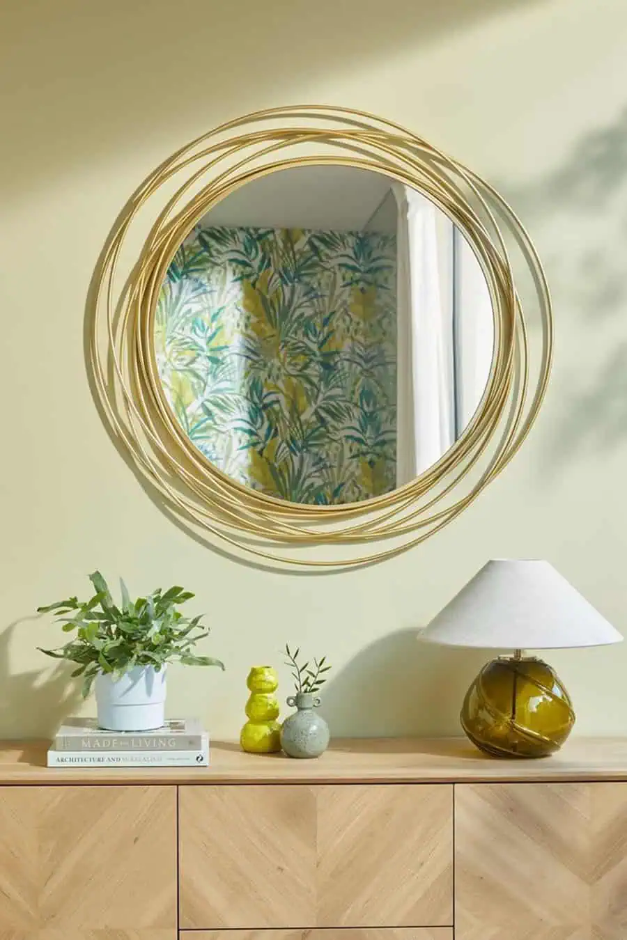 Decorative gold-edged mirror above a wooden console with vibrant plants and modern decor.