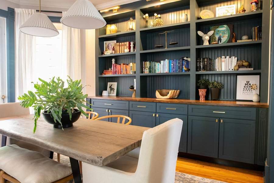 Dining room with built-in home library, navy shelves, and a rustic wooden table.