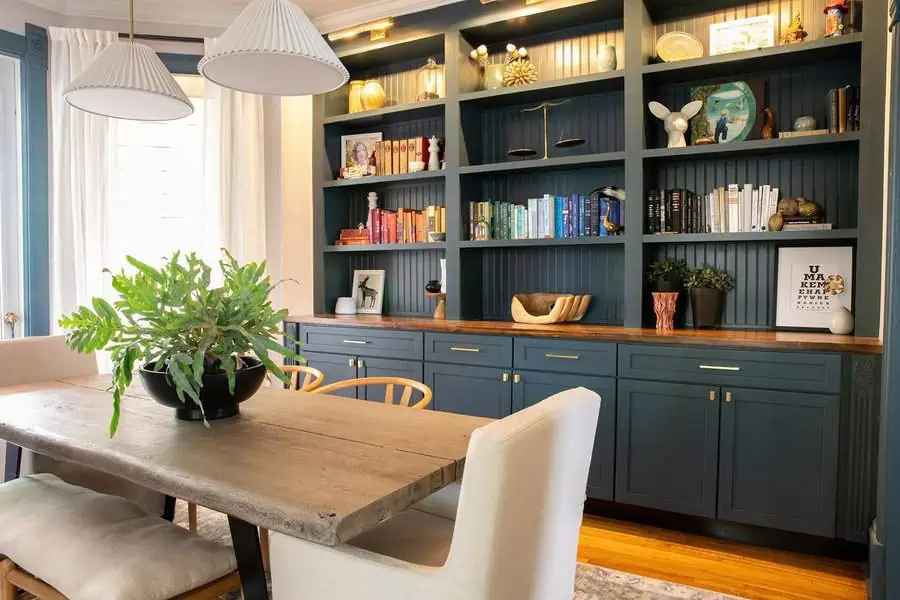 Dining room with built-in home library, navy shelves, and a rustic wooden table.