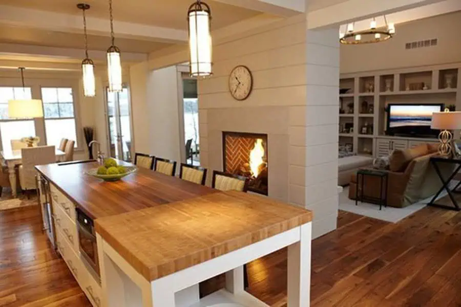 Open kitchen with a large wood island, pendant lighting, and a double-sided fireplace.