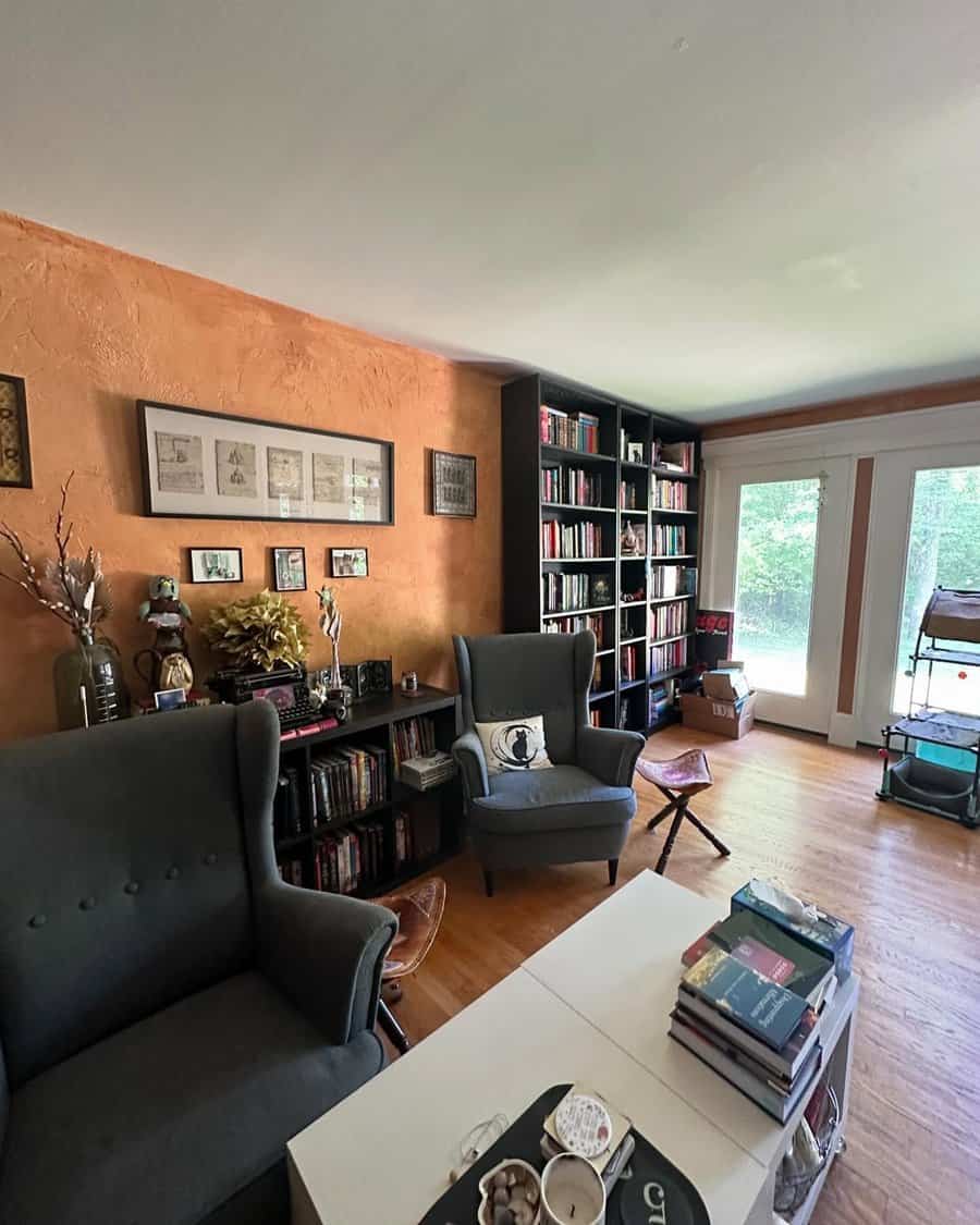 Cozy home library with dark bookshelves, wingback chairs, and warm-toned textured walls.