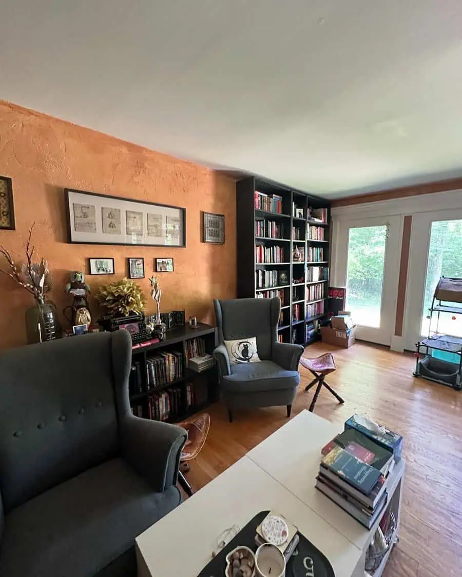 Cozy home library with dark bookshelves, wingback chairs, and warm-toned textured walls.