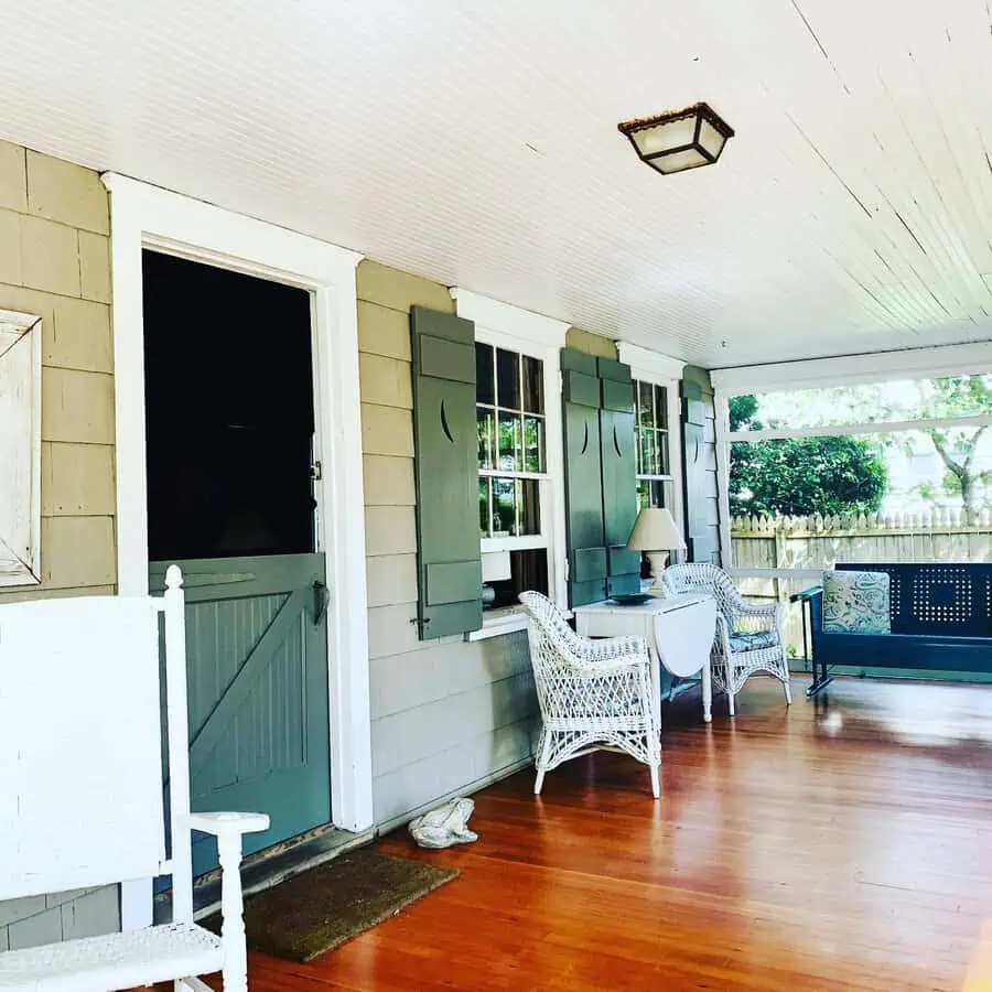 Dutch Colonial house porch with a Dutch door, wooden flooring, wicker chairs, and green shutters.