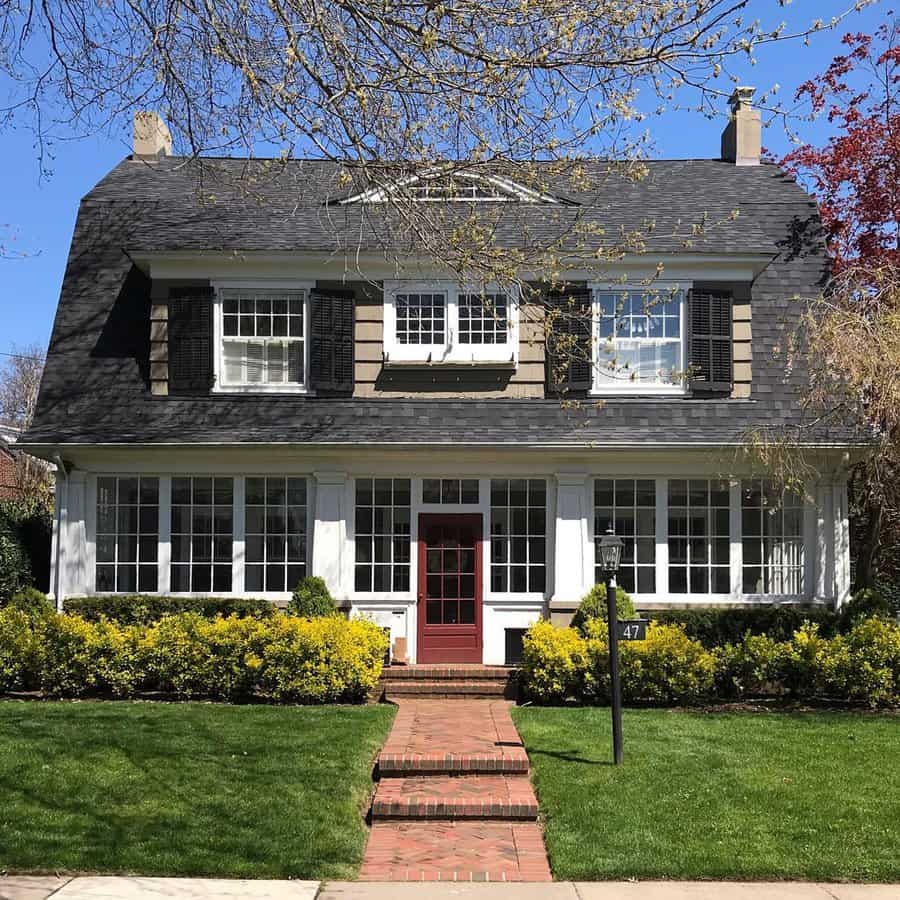 Dutch Colonial house with a gambrel roof, enclosed front porch, red door, and classic shutters.