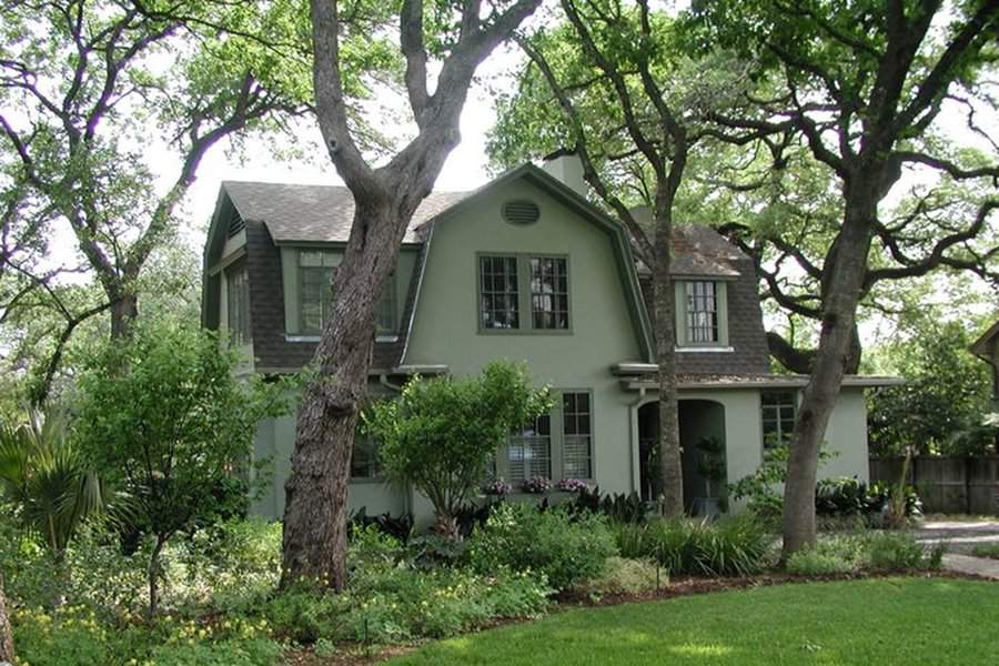 Dutch Colonial house with a stucco finish, gambrel roof, and lush garden surroundings.