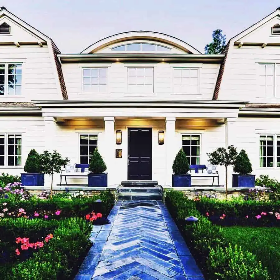 Dutch Colonial house with a gambrel roof, black front door, manicured landscaping, and stylish curb appeal.