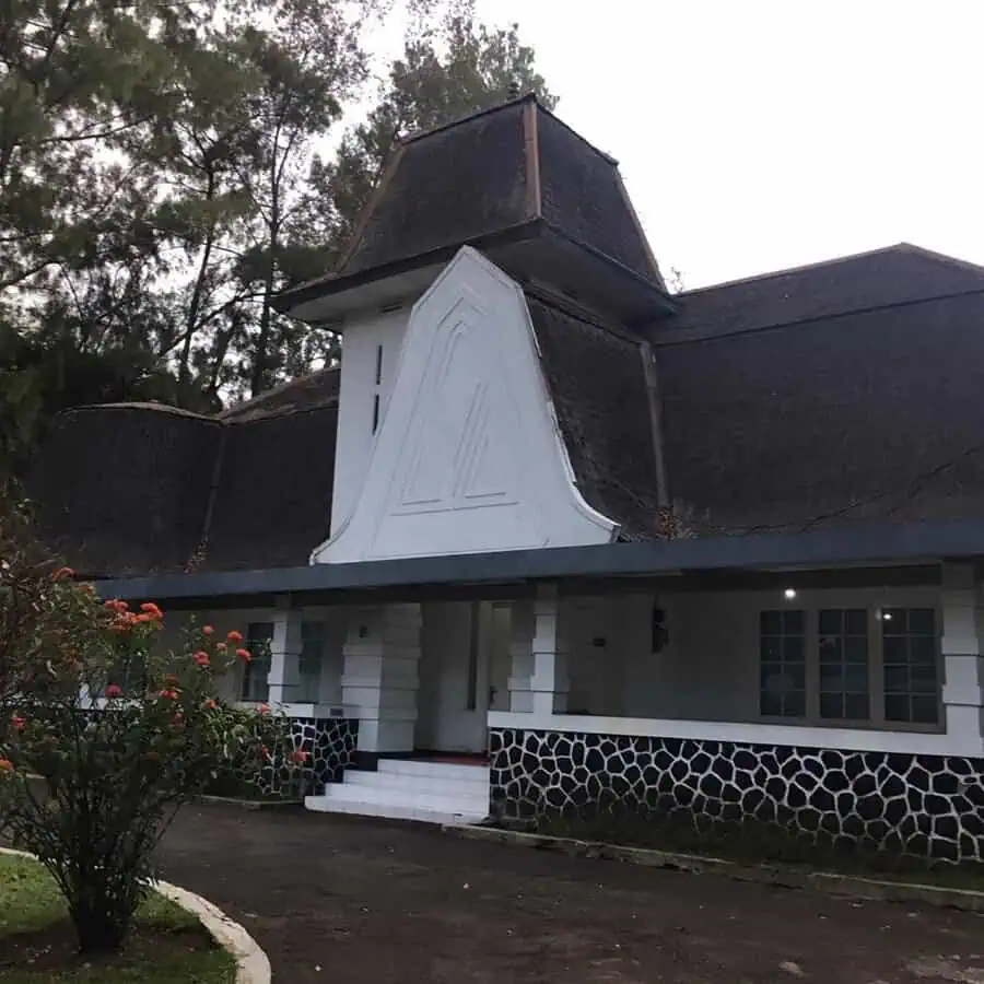 Dutch Colonial house with a tiered gambrel roof, white facade, and black stone foundation.