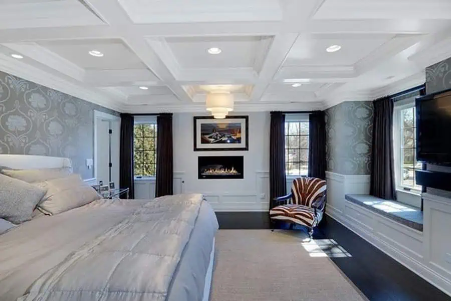 Elegant master bedroom with a modern coffered ceiling, fireplace, plush bedding, and stylish decor.