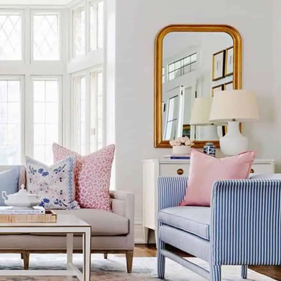 Gold-framed mirror above a white console reflecting a bright and elegant living room.