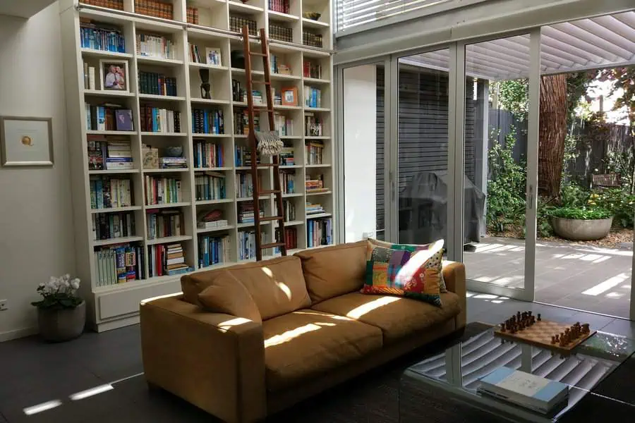 Bright living room with a floor-to-ceiling bookshelf, library ladder, and cozy seating area.