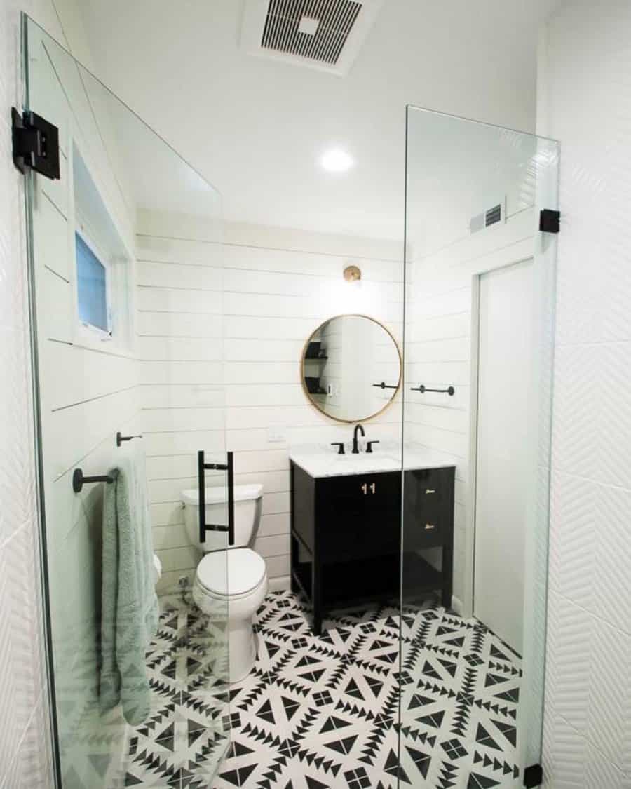 Black and white bathroom with glossy black cabinets, white countertops, and geometric floor tiles.