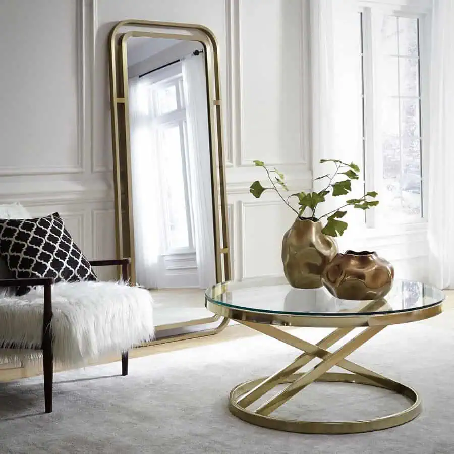 Tall gold-framed mirror beside a sleek glass coffee table in an elegant living room.