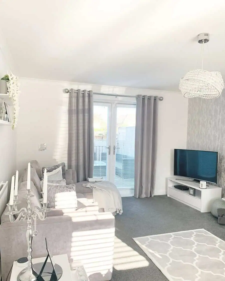 Bright grey and white living room with soft drapes, a plush sofa, and a crystal chandelier.