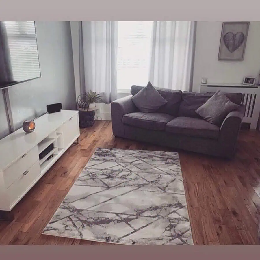 Grey and white living room with a cozy sofa, marble-patterned rug, and sheer drapes.