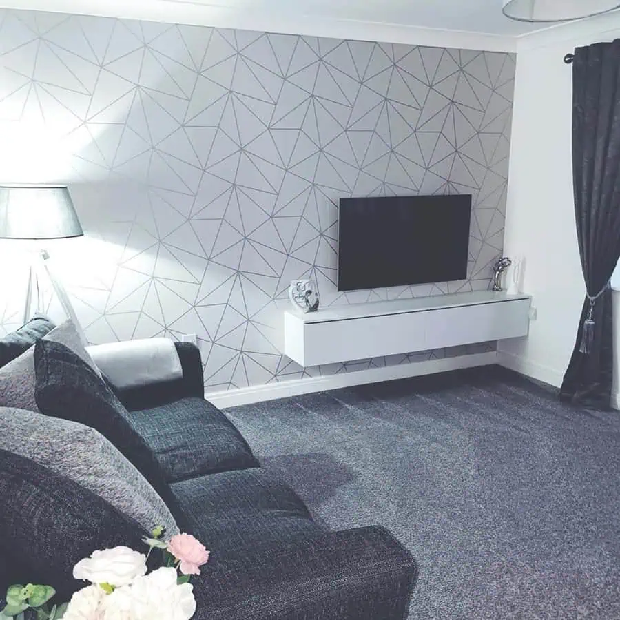 Grey and white living room with a geometric accent wall, dark sofa, and mounted TV.