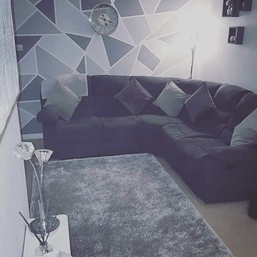 Grey and white living room with a geometric accent wall, plush sectional sofa, and cozy decor.