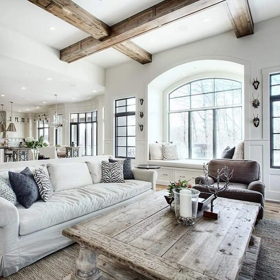 Grey and white living room with rustic wood beams, large windows, and a reclaimed wood coffee table.