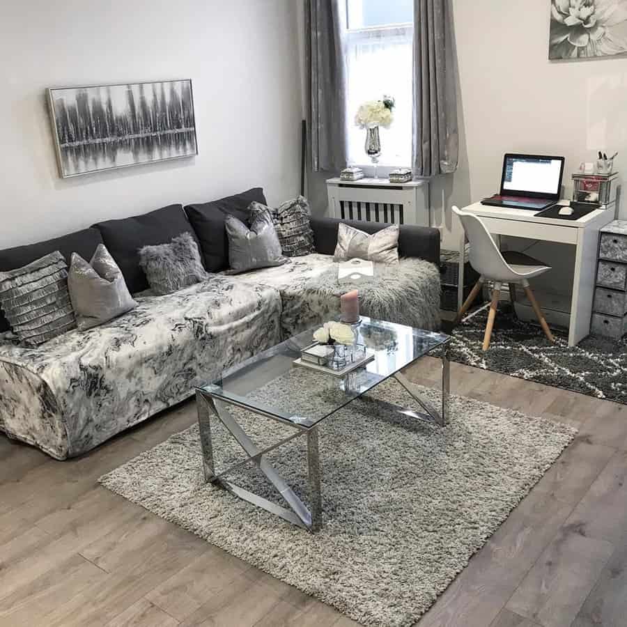 Grey and white living room with a cozy sofa, glass coffee table, and a small home office setup.