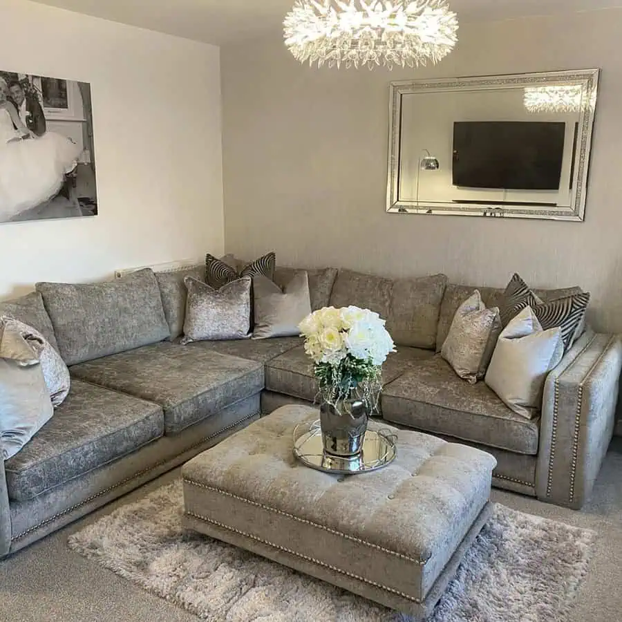 Elegant grey and white living room with a plush sectional sofa, tufted ottoman, and crystal chandelier.