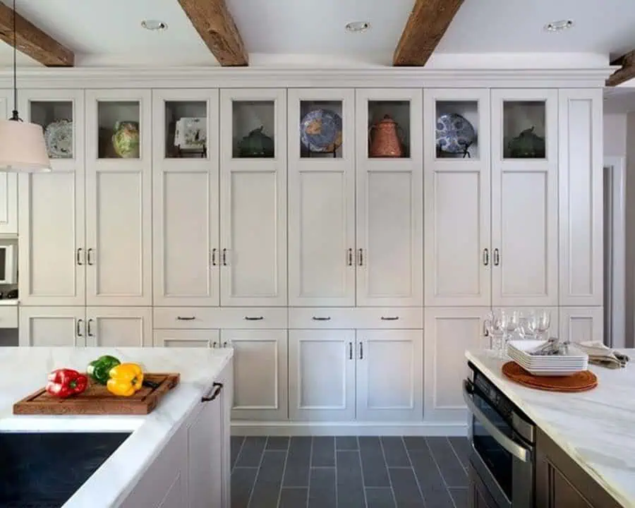 High-ceiling open kitchen with floor-to-ceiling cabinetry, exposed wood beams, and a marble island.