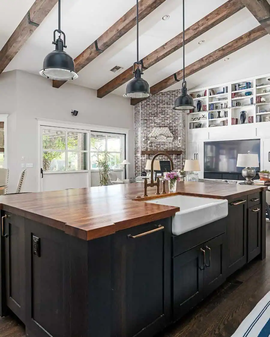 Rustic open kitchen with exposed beams, black pendant lights, and a large wooden island.