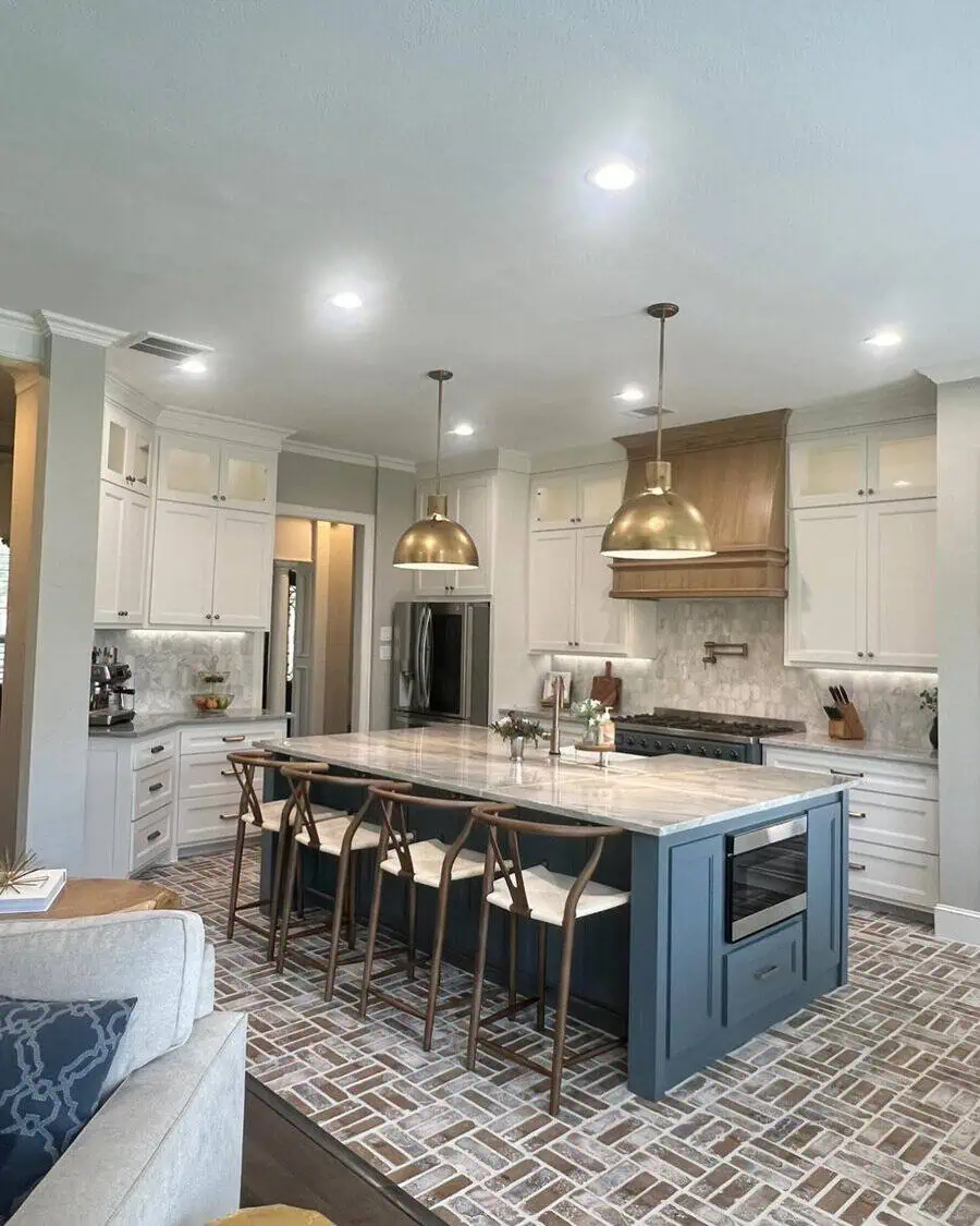 Open kitchen with high ceilings, a blue island, brass pendant lights, and brick flooring.