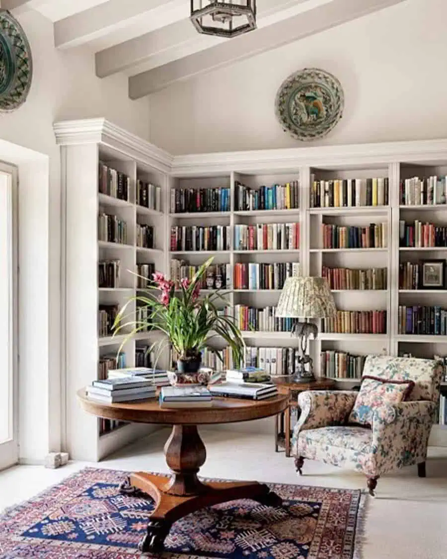 Elegant home library with built-in bookshelves, a vintage round table, and a cozy floral armchair.