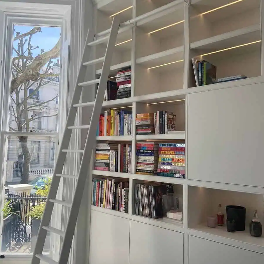 Home library with built-in white bookshelves, a rolling ladder, and a functional furniture setup.