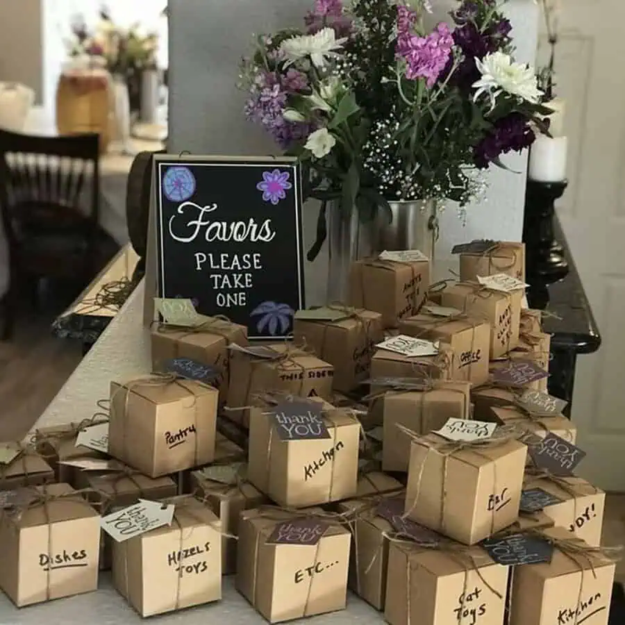 Housewarming party favor table with personalized gift boxes, a chalkboard sign, and floral decor.