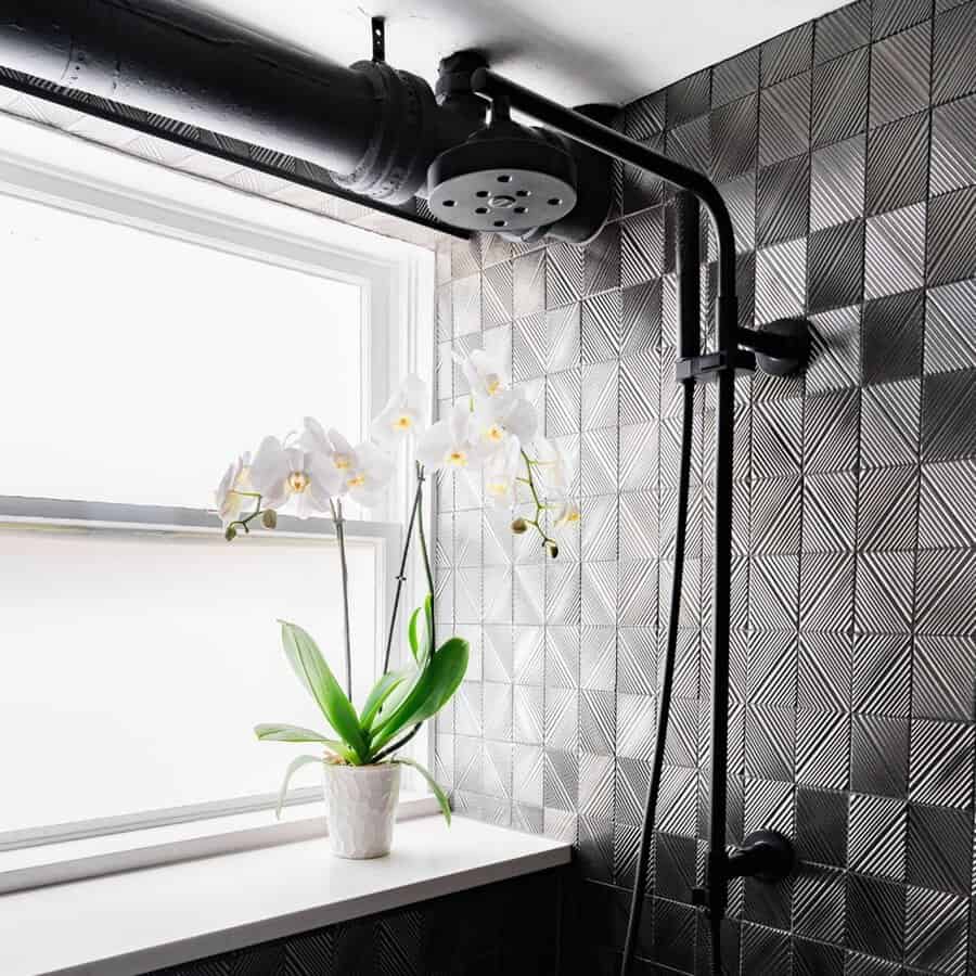 Industrial black bathroom with textured tiles, matte black shower fixtures, and a white orchid.