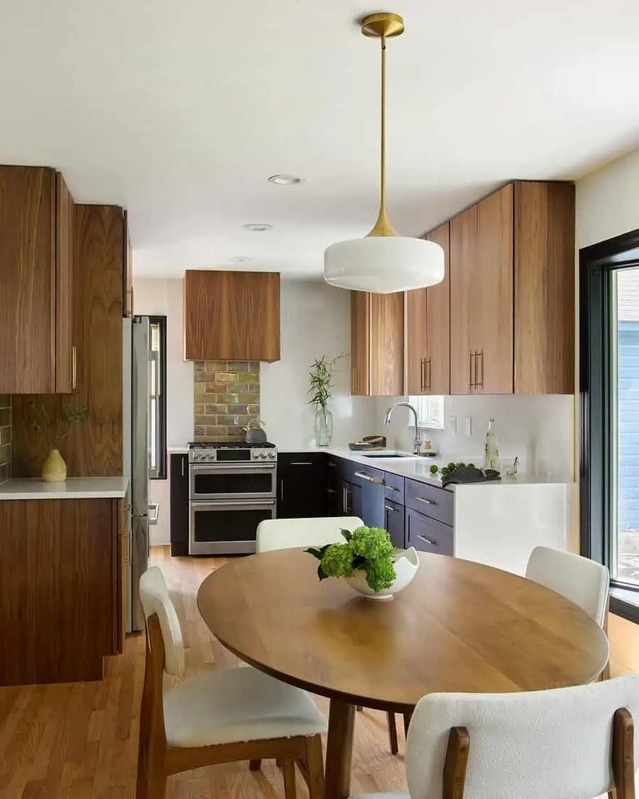 Integrated open kitchen with wood cabinetry, a round dining table, and modern pendant lighting.