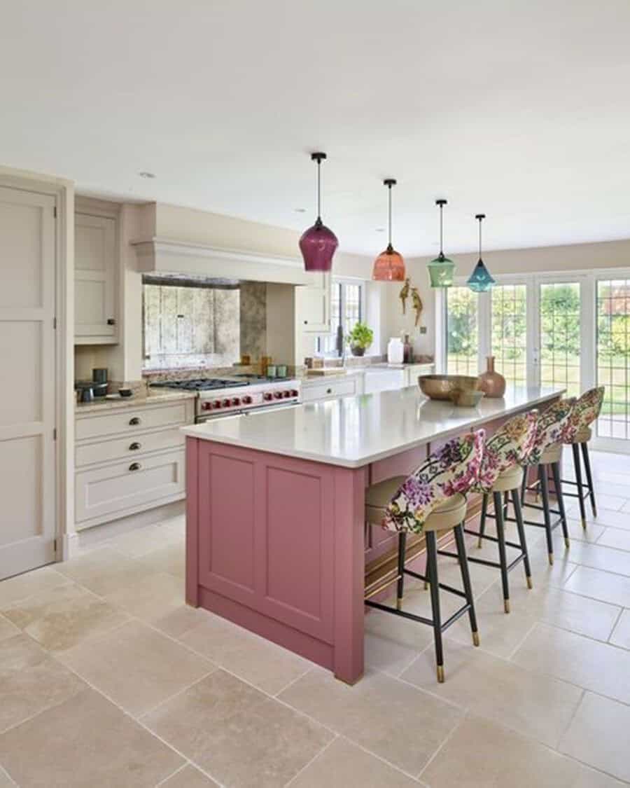 Open kitchen with a pink island, colorful pendant lights, and floral-patterned bar stools.