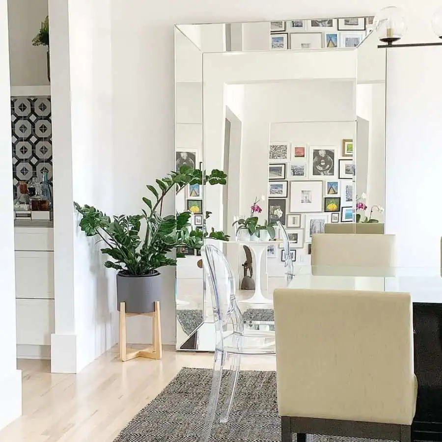 Large frameless mirror reflecting a gallery wall in a modern dining room with neutral decor.