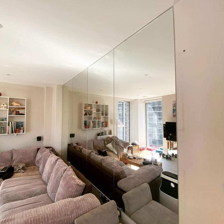 Wall-to-wall frameless mirrors reflecting a modern living room with a cozy sectional sofa.