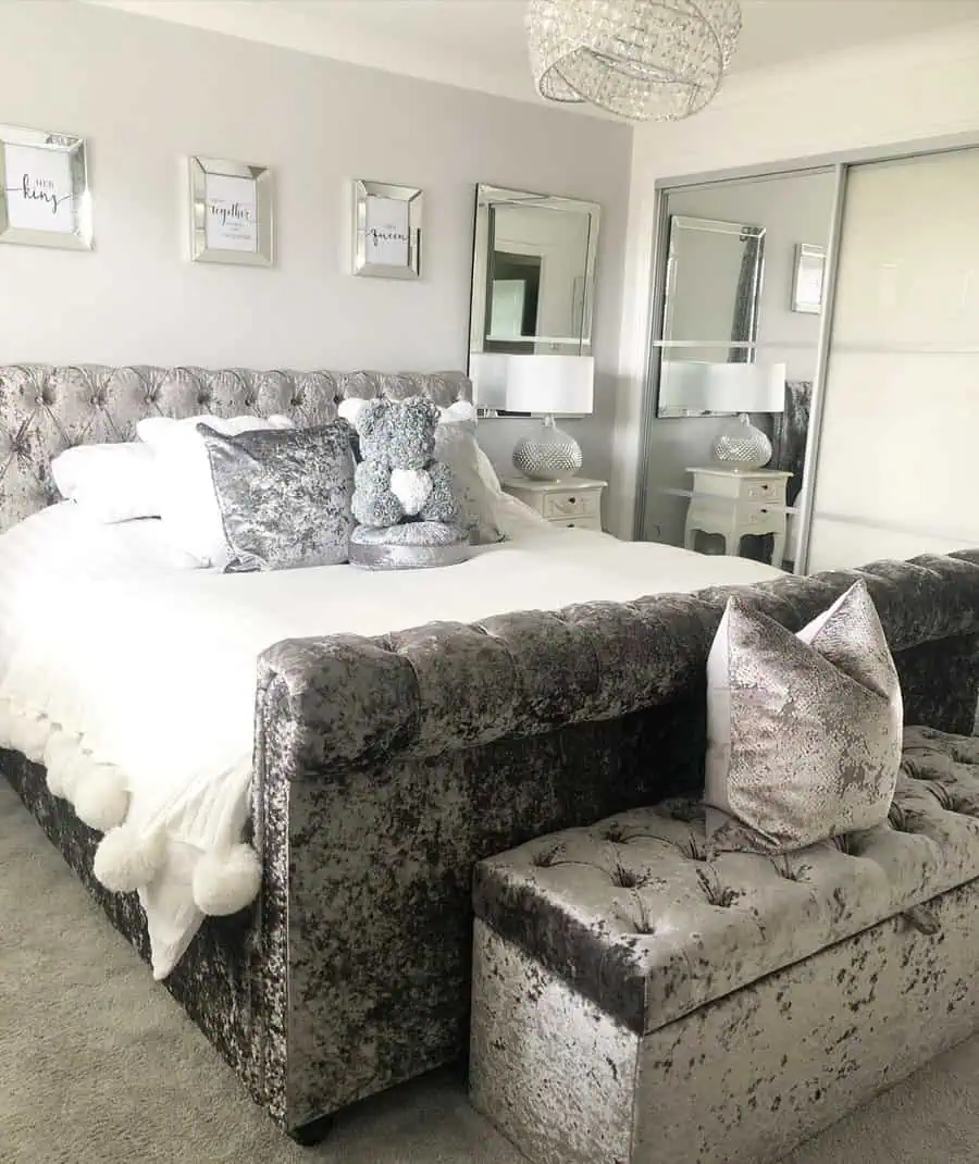 Luxurious grey and white bedroom with a velvet tufted bed, mirrored decor, and crystal lighting.