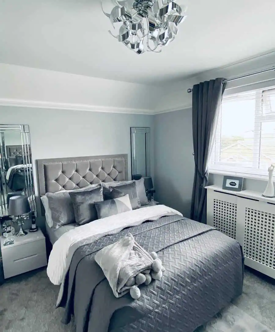 Luxury grey and white bedroom with a tufted headboard, mirrored decor, and elegant lighting.