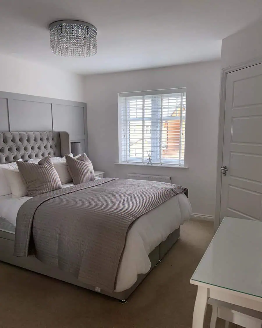 Elegant bedroom with a tufted headboard, soft neutral bedding, and a crystal chandelier.