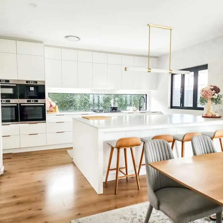 Modern minimalist kitchen with white cabinetry, a sleek island, wood accents, and natural light.