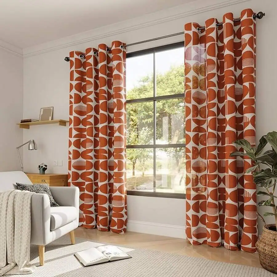 Modern bedroom with bold orange geometric curtains, cozy seating, and natural light-filled space.