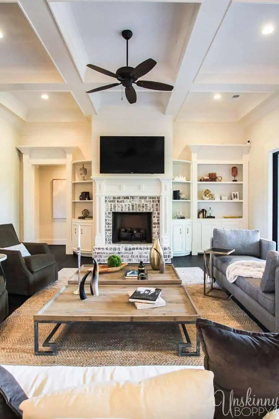 Modern farmhouse living room with a coffered ceiling, brick fireplace, built-in shelves, and cozy seating.