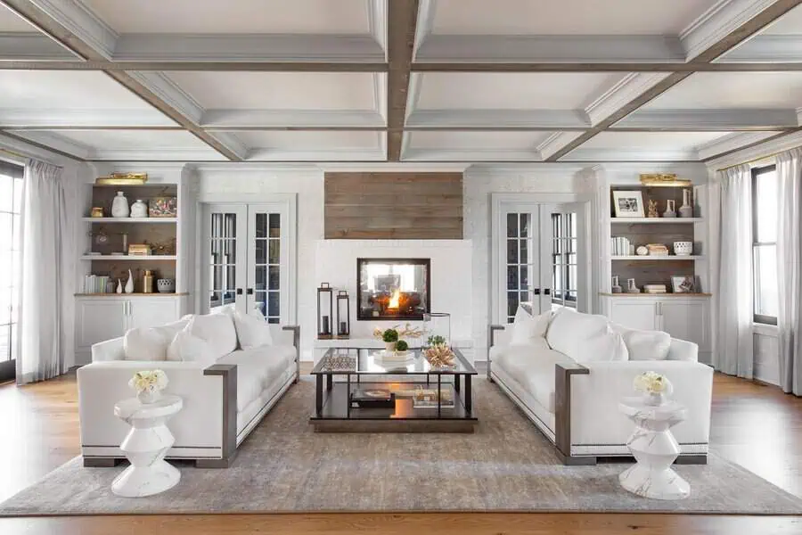 Modern farmhouse living room with a coffered ceiling, white sofas, a fireplace, and built-in shelves.