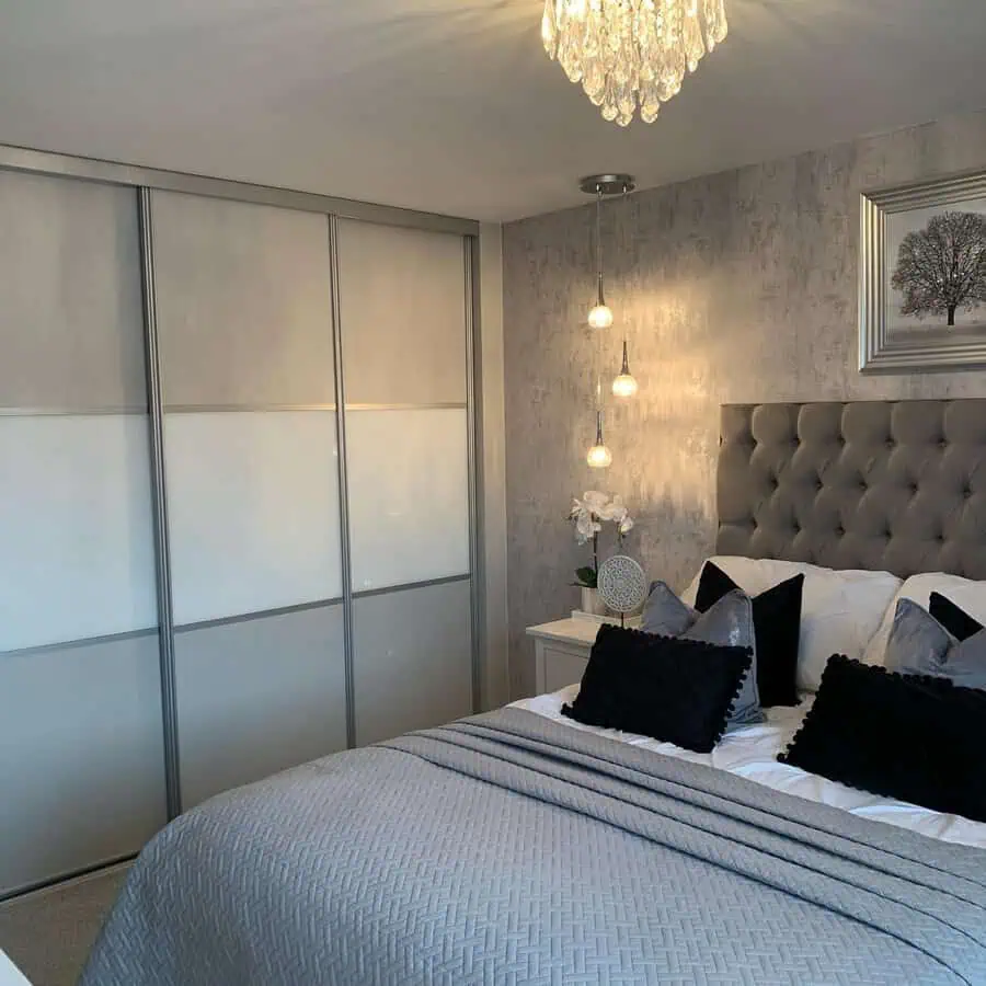 Stylish grey and white bedroom with a tufted headboard, pendant lights, and a crystal chandelier.